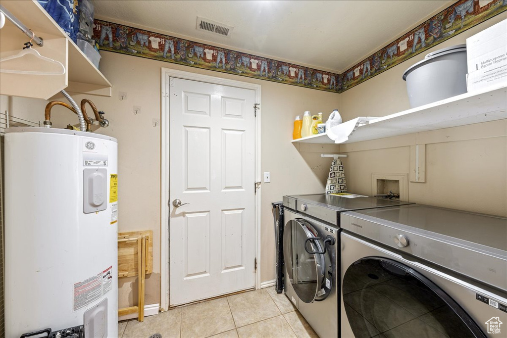 Laundry area featuring electric water heater, washer and clothes dryer, and light tile patterned floors