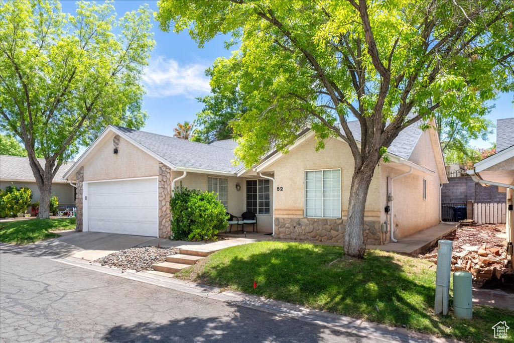 Ranch-style house with stone siding, an attached garage, stucco siding, and driveway