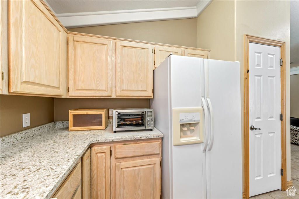 Kitchen featuring white fridge with ice dispenser, light brown cabinets, vaulted ceiling, and light stone counters