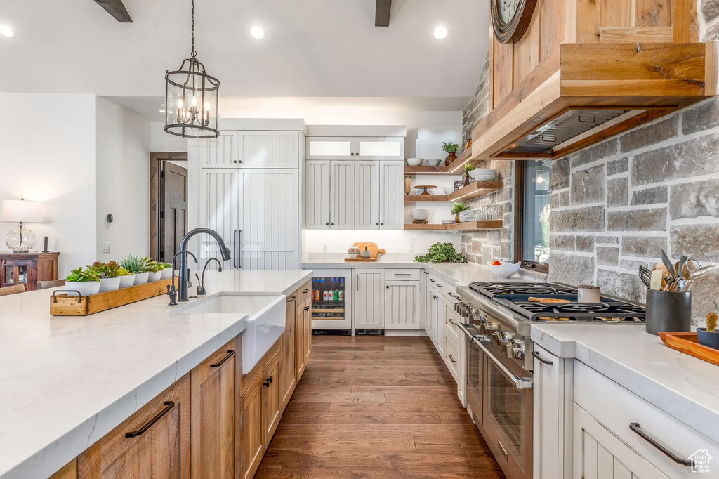Kitchen featuring double oven range, beverage cooler, under cabinet range hood, a sink, and tasteful backsplash