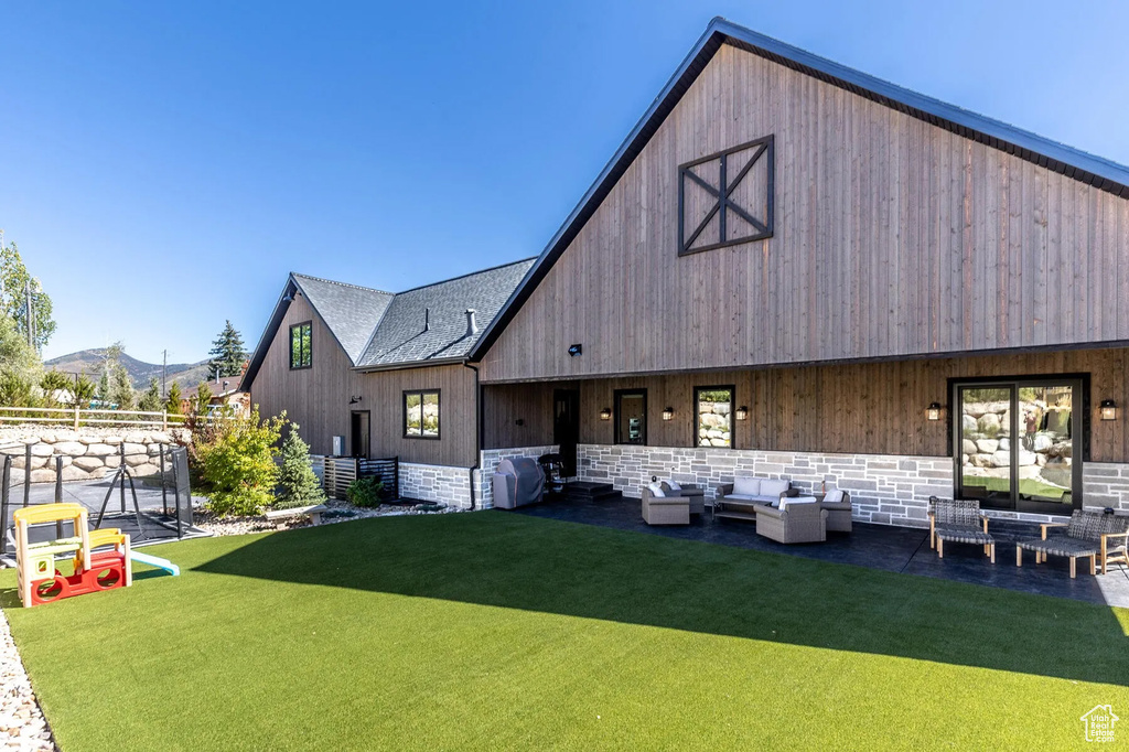 Back of property with an outdoor living space, a lawn, stone siding, a mountain view, and a barn