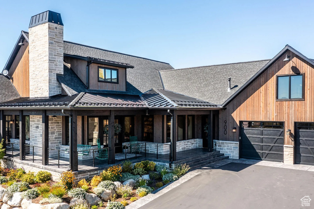 View of front facade featuring a chimney, covered porch, driveway, and a standing seam roof