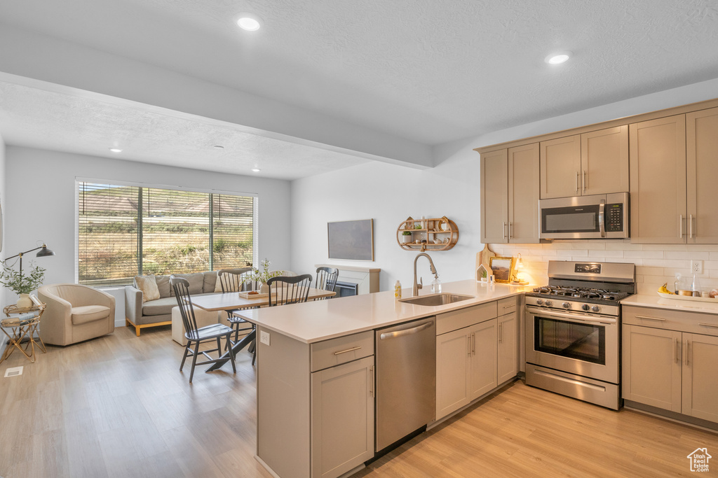 Kitchen with stainless steel appliances, a sink, a peninsula, light countertops, and open floor plan
