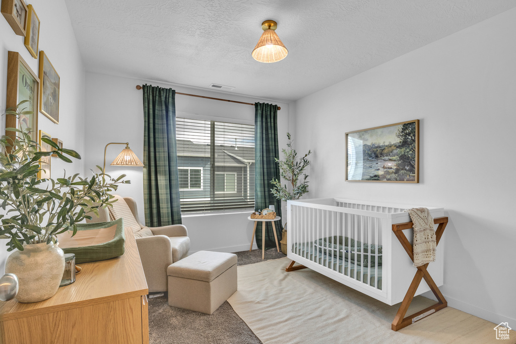 Bedroom featuring a nursery area, a textured ceiling, baseboards, and carpet floors