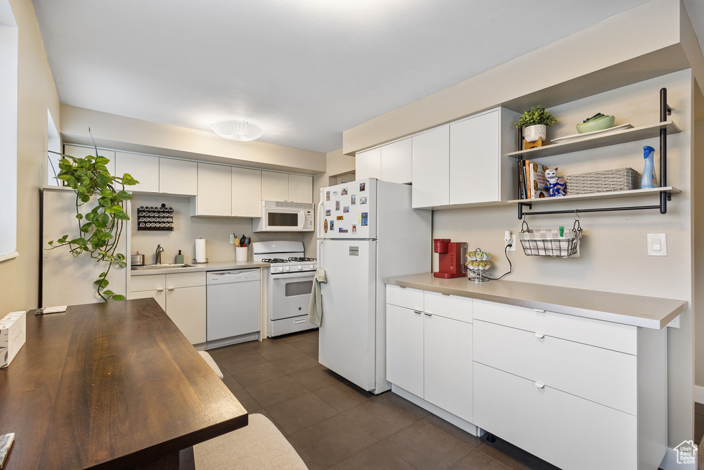Kitchen with white appliances, a sink, dark tile patterned flooring, and light countertops