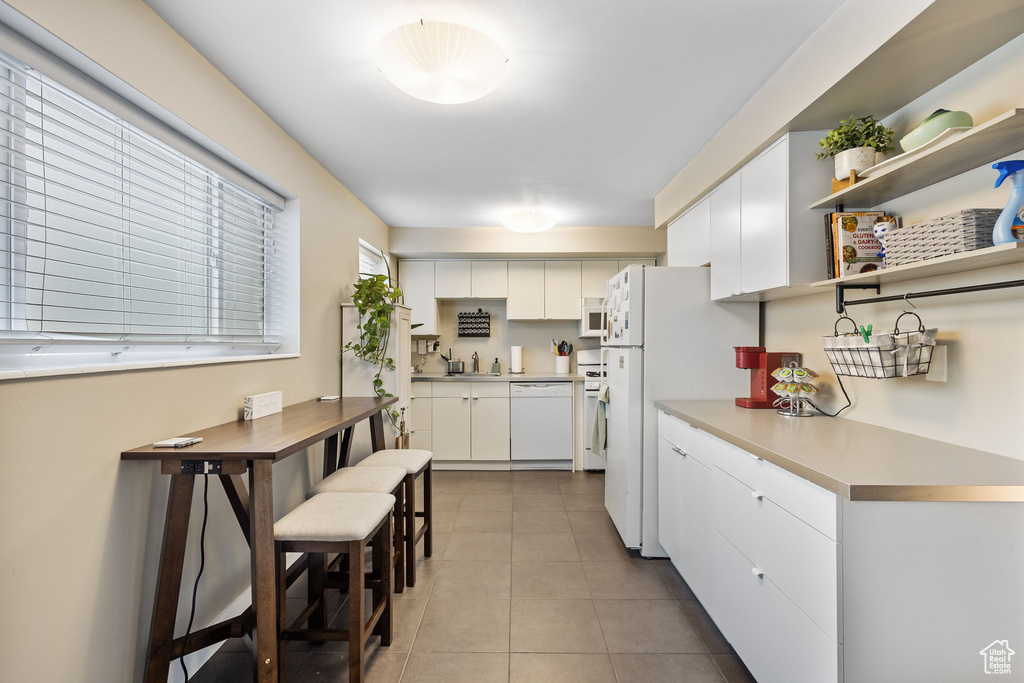 Kitchen with white appliances, white cabinets, a sink, and light tile patterned floors