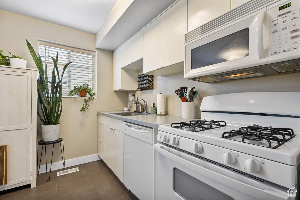 Kitchen featuring white appliances, a sink, light countertops, and white cabinetry