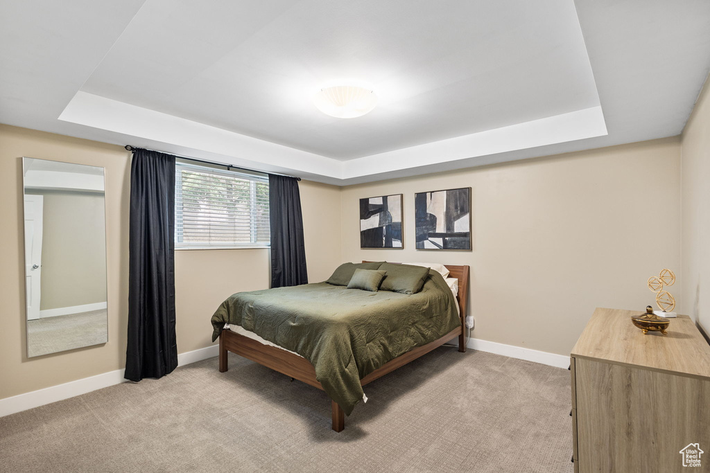 Bedroom with a tray ceiling, light colored carpet, and baseboards