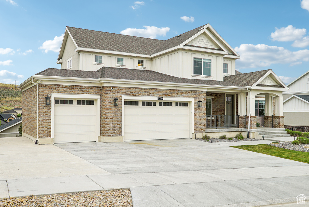 View of front of home with covered porch, board and batten siding, driveway, brick siding, and a garage