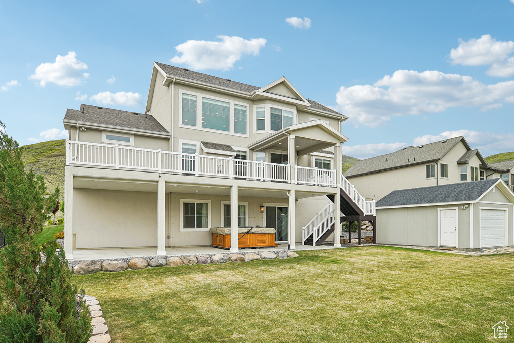 Rear view of house featuring a hot tub, stucco siding, an outbuilding, and a yard