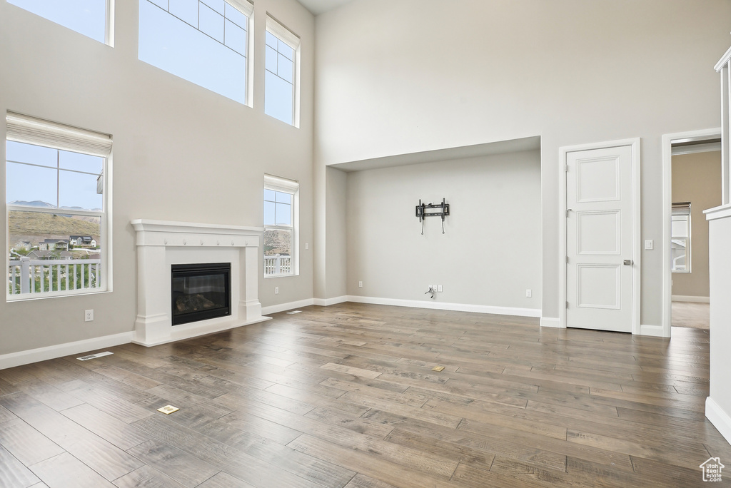Unfurnished living room featuring a towering ceiling, plenty of natural light, a glass covered fireplace, wood finished floors, and baseboards
