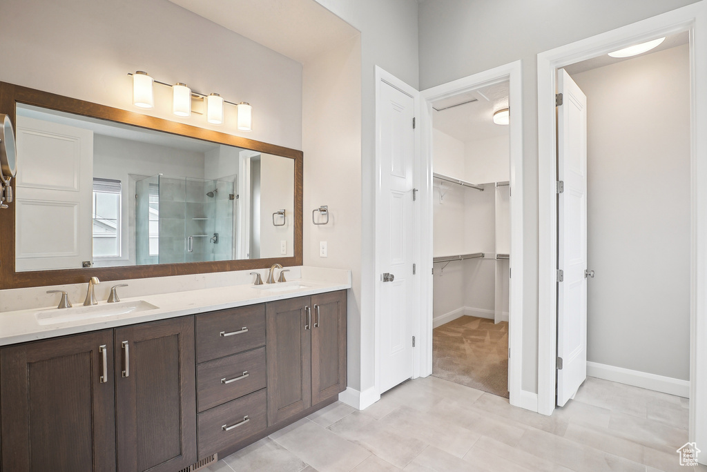 Bathroom with a stall shower, a walk in closet, double vanity, baseboards, and tile patterned flooring