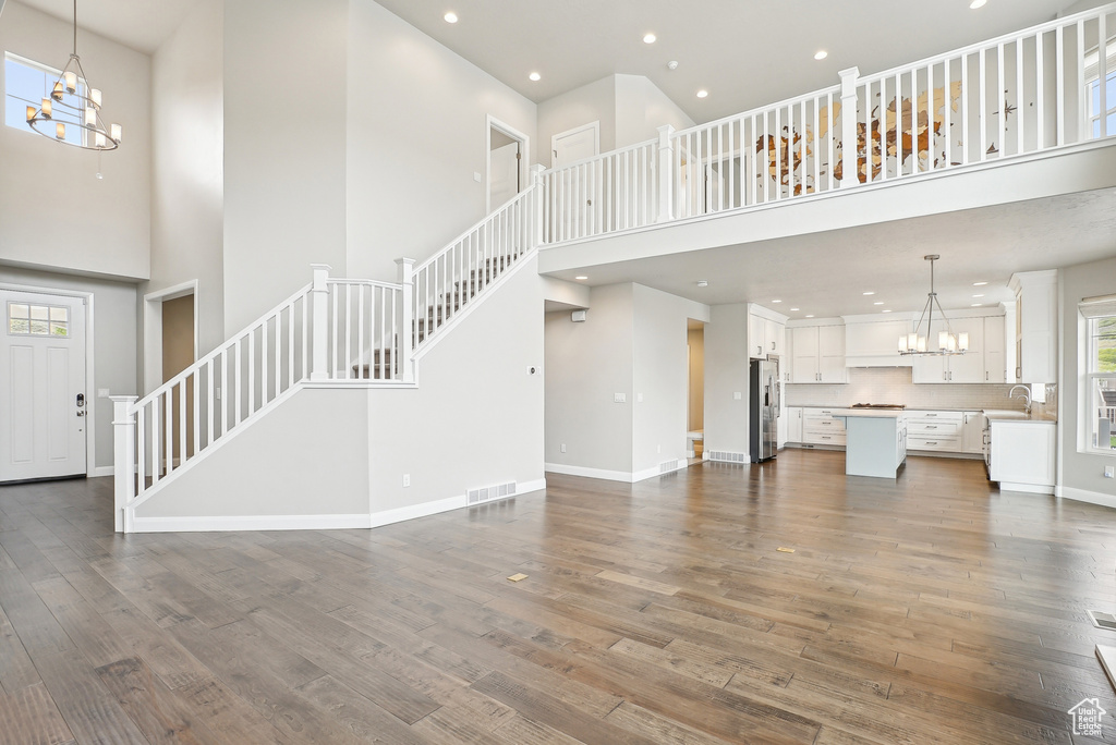 Unfurnished living room featuring a chandelier, a high ceiling, stairway, a sink, and dark wood finished floors