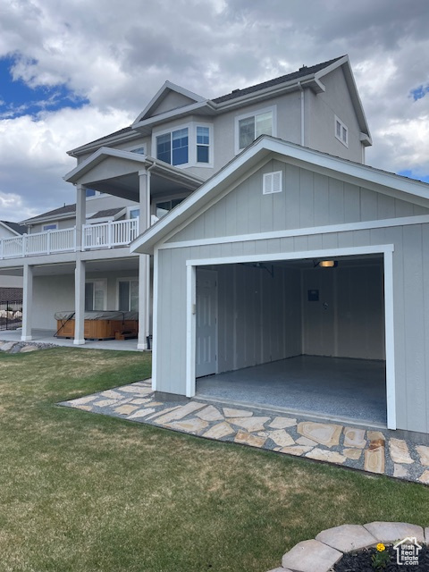 View of front facade with a hot tub, a garage, a front yard, and a balcony