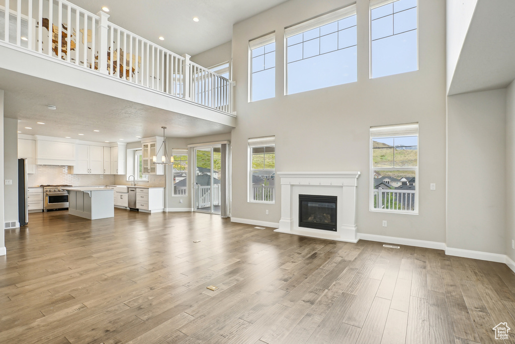 Unfurnished living room with a high ceiling, wood finished floors, a glass covered fireplace, baseboards, and recessed lighting