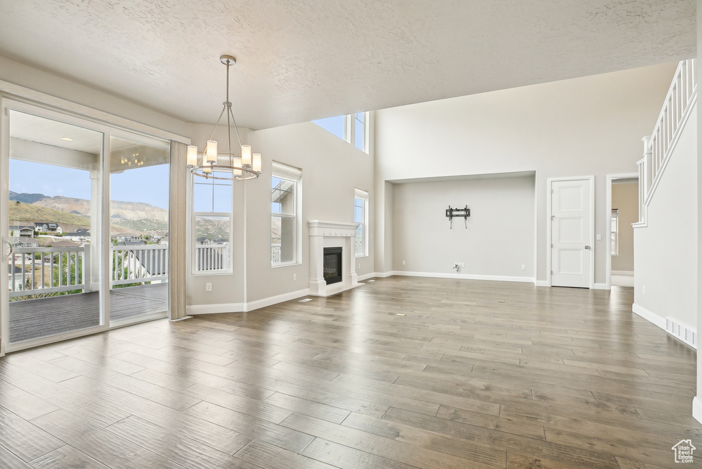 Unfurnished living room featuring a chandelier, hardwood / wood-style flooring, a textured ceiling, baseboards, and a glass covered fireplace