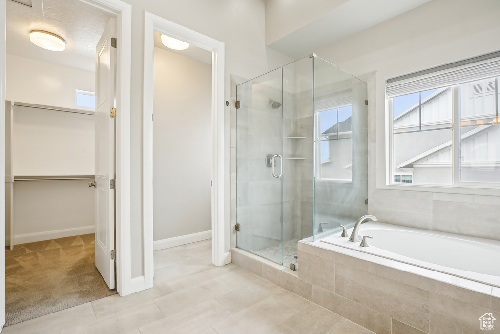 Full bathroom with a shower stall, a walk in closet, a bath, tile patterned flooring, and baseboards