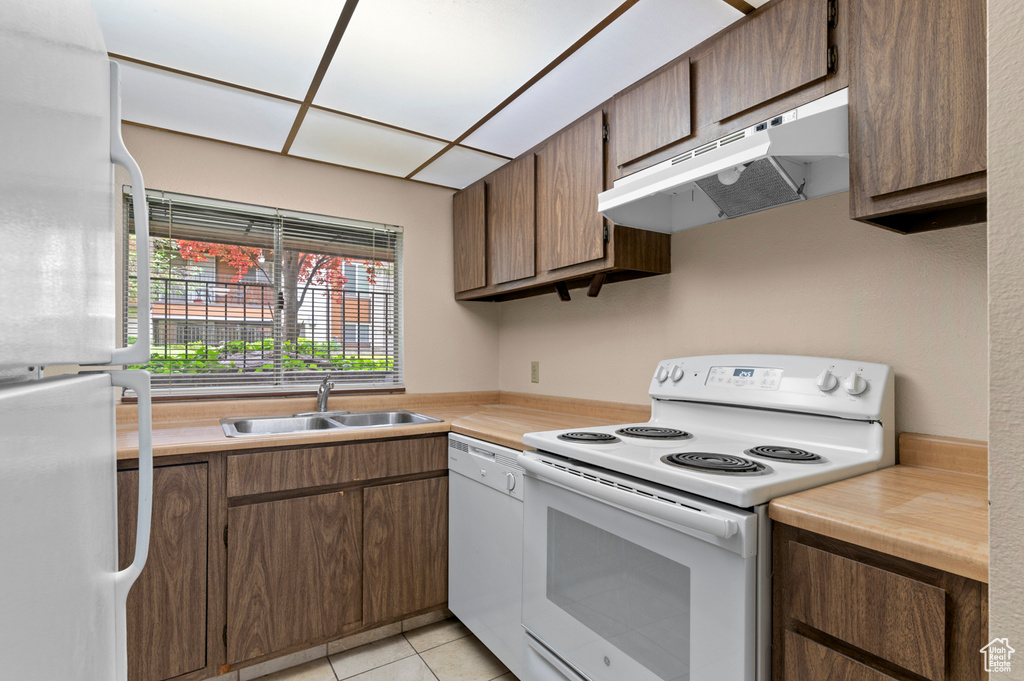 Kitchen featuring white appliances, under cabinet range hood, a sink, and light countertops