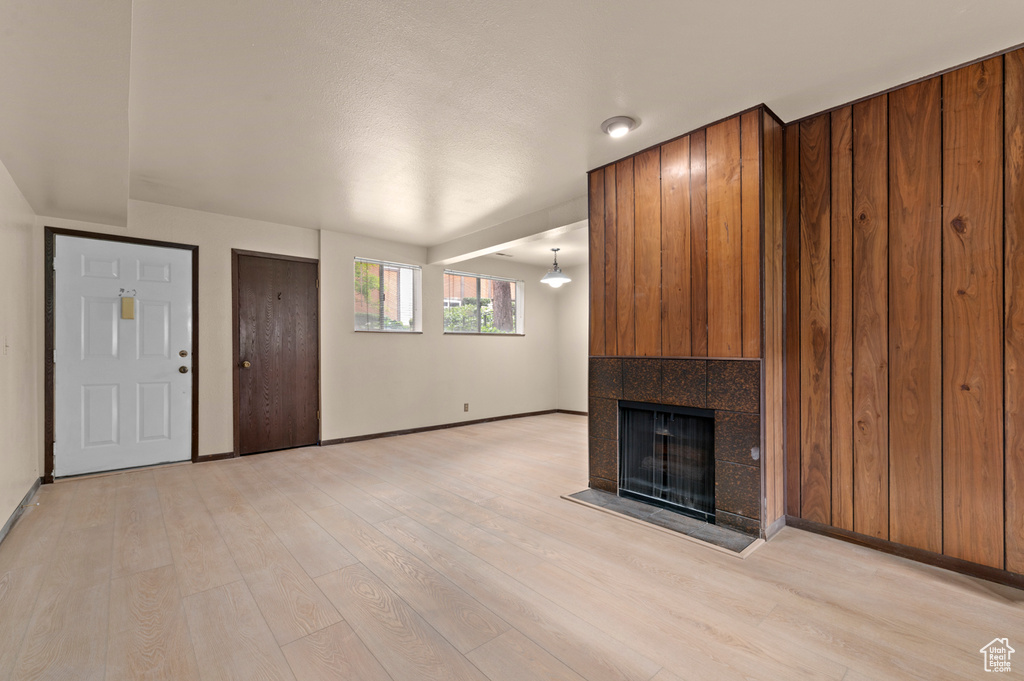 Unfurnished living room featuring baseboards, light wood-type flooring, and a tiled fireplace