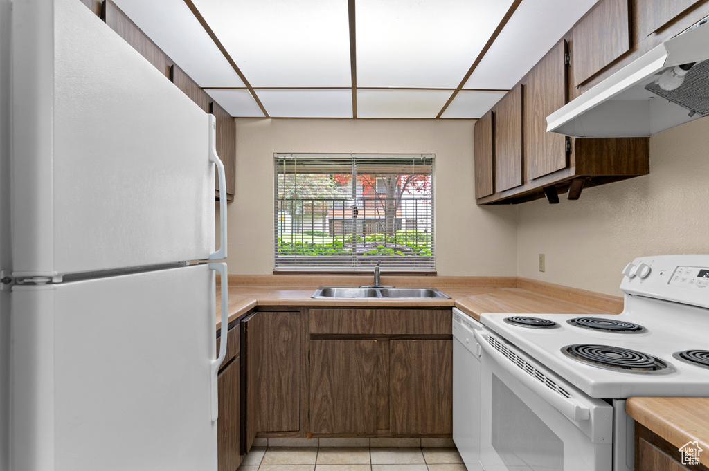 Kitchen with white appliances, under cabinet range hood, a sink, and light countertops