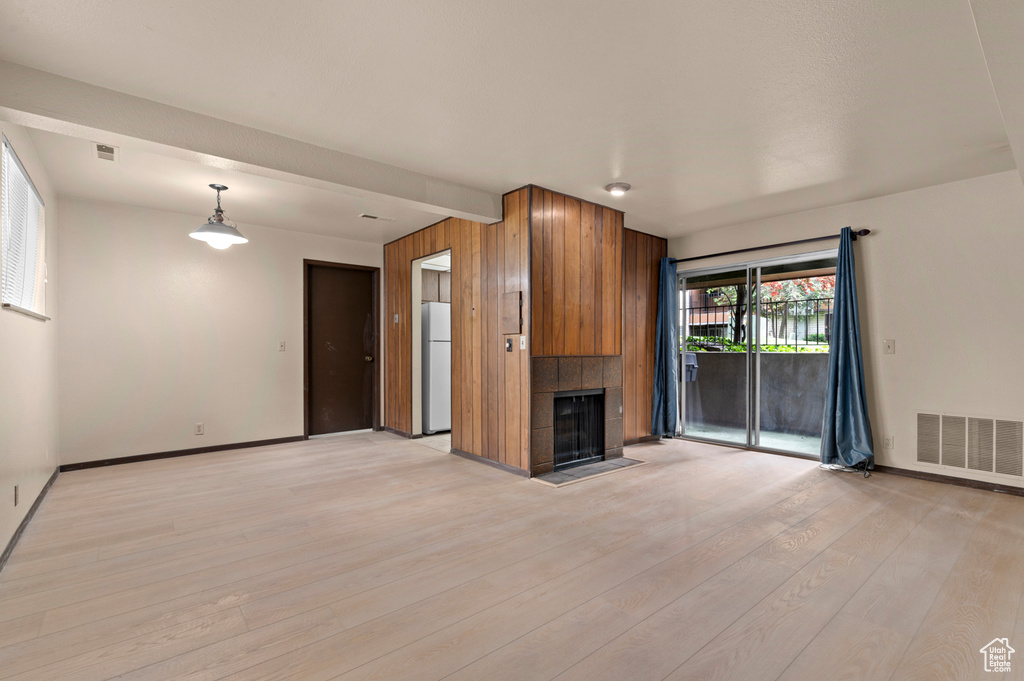 Unfurnished living room with baseboards, light wood-type flooring, and a tiled fireplace