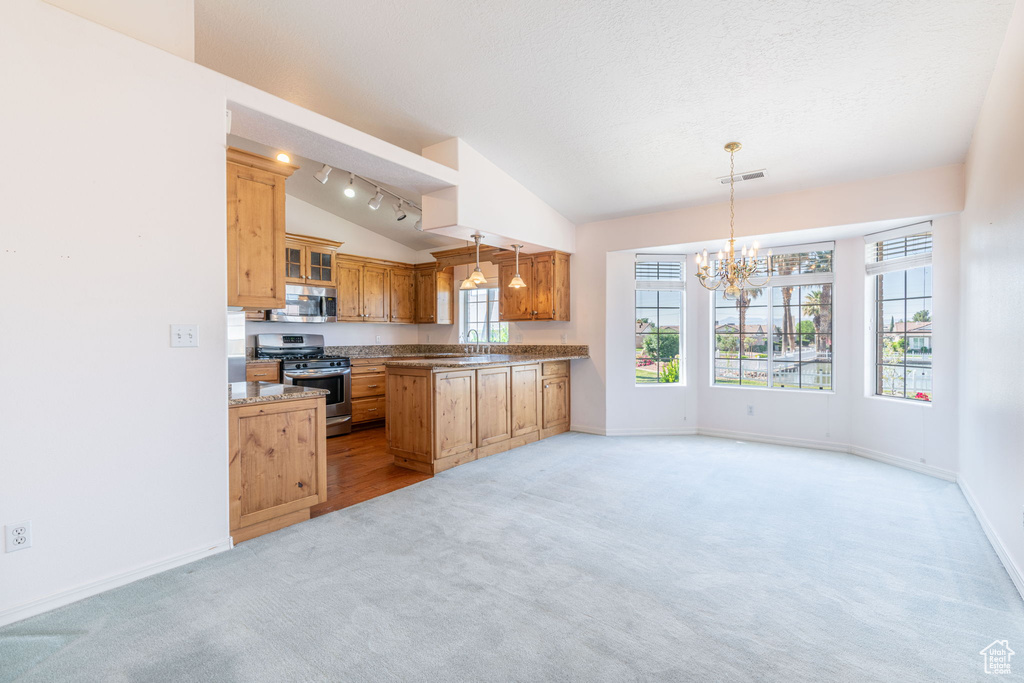 Kitchen with stainless steel appliances, lofted ceiling, light colored carpet, a chandelier, and baseboards