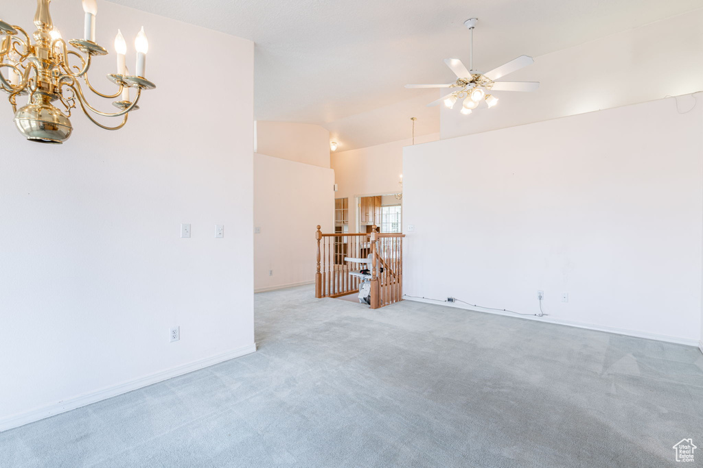Unfurnished room featuring light colored carpet, lofted ceiling, a ceiling fan, a chandelier, and baseboards