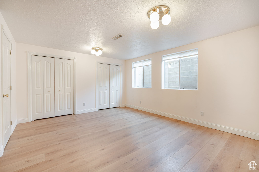 Unfurnished bedroom featuring light wood finished floors, two closets, baseboards, and a textured ceiling