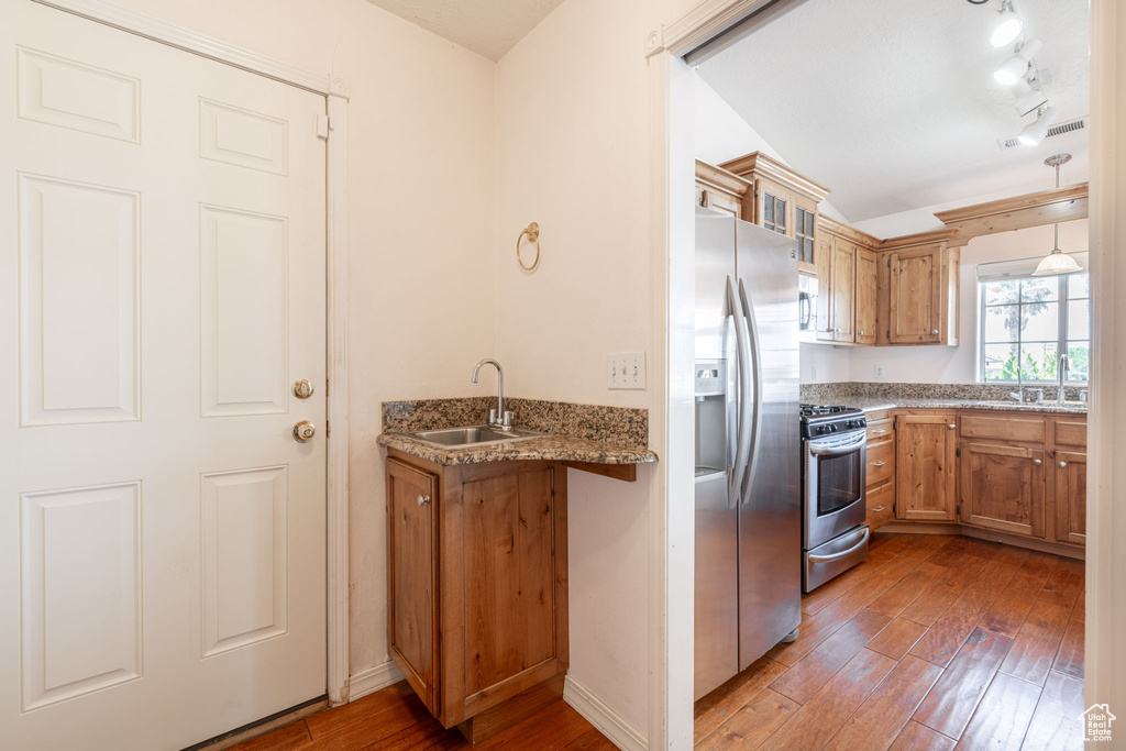 Kitchen with appliances with stainless steel finishes, hardwood / wood-style floors, a sink, brown cabinetry, and light stone counters