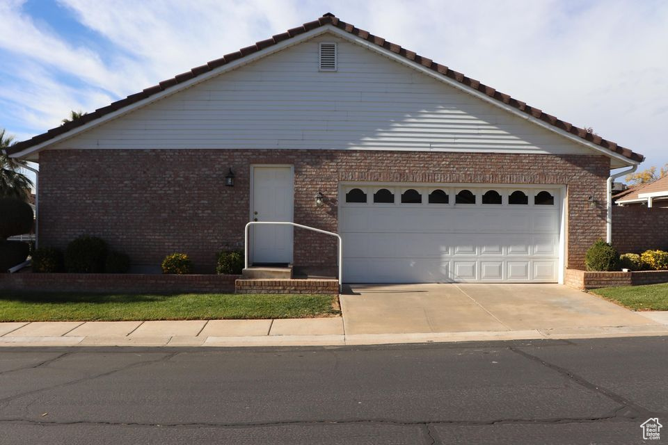 Ranch-style home with concrete driveway, brick siding, a tile roof, and an attached garage