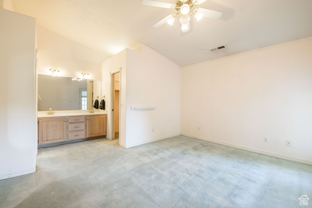 Unfurnished bedroom with lofted ceiling, a sink, light carpet, baseboards, and connected bathroom
