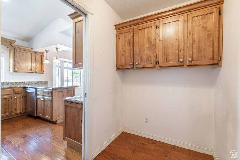 Kitchen with vaulted ceiling, stainless steel dishwasher, dark wood-type flooring, a peninsula, and baseboards