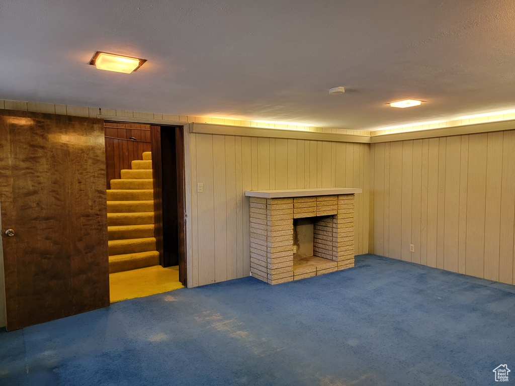 Finished below grade area with carpet, wooden walls, stairs, and a brick fireplace