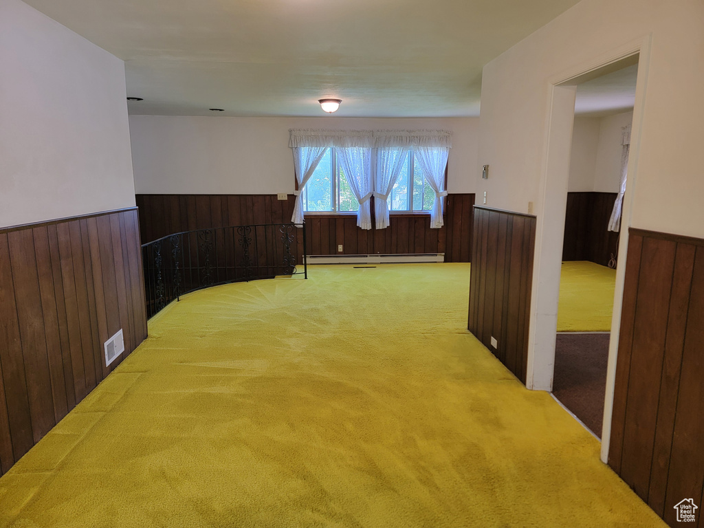 Unfurnished room with a wainscoted wall, carpet, a baseboard radiator, and wood walls