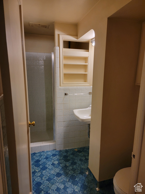 Bathroom featuring tile walls, a stall shower, and toilet
