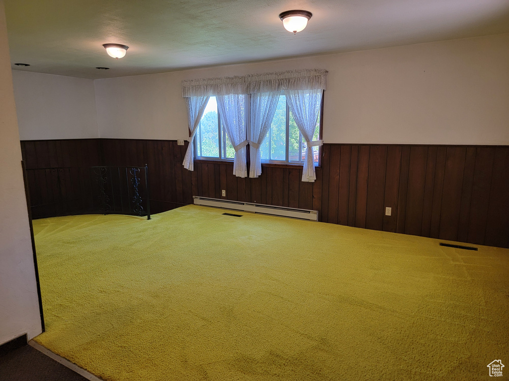 Spare room featuring baseboard heating, carpet, a wainscoted wall, and wood walls