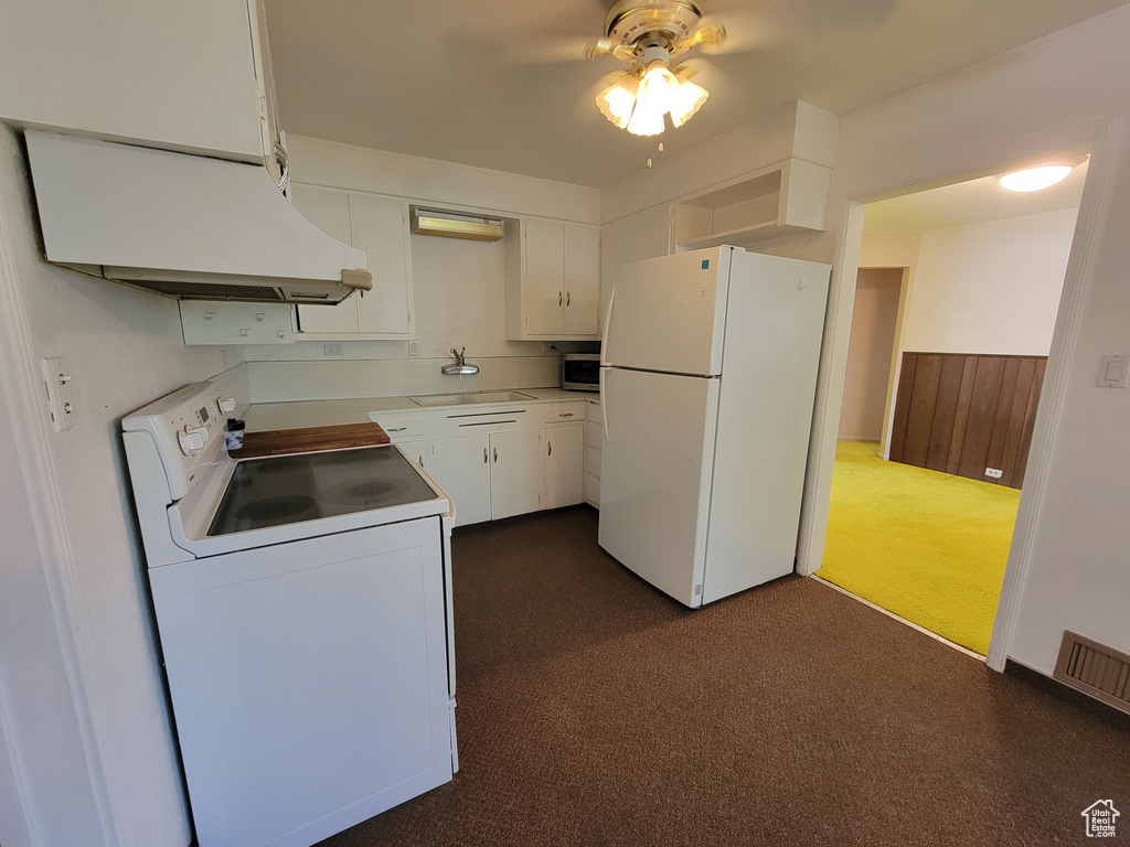 Kitchen with white appliances, under cabinet range hood, ceiling fan, dark colored carpet, and white cabinetry