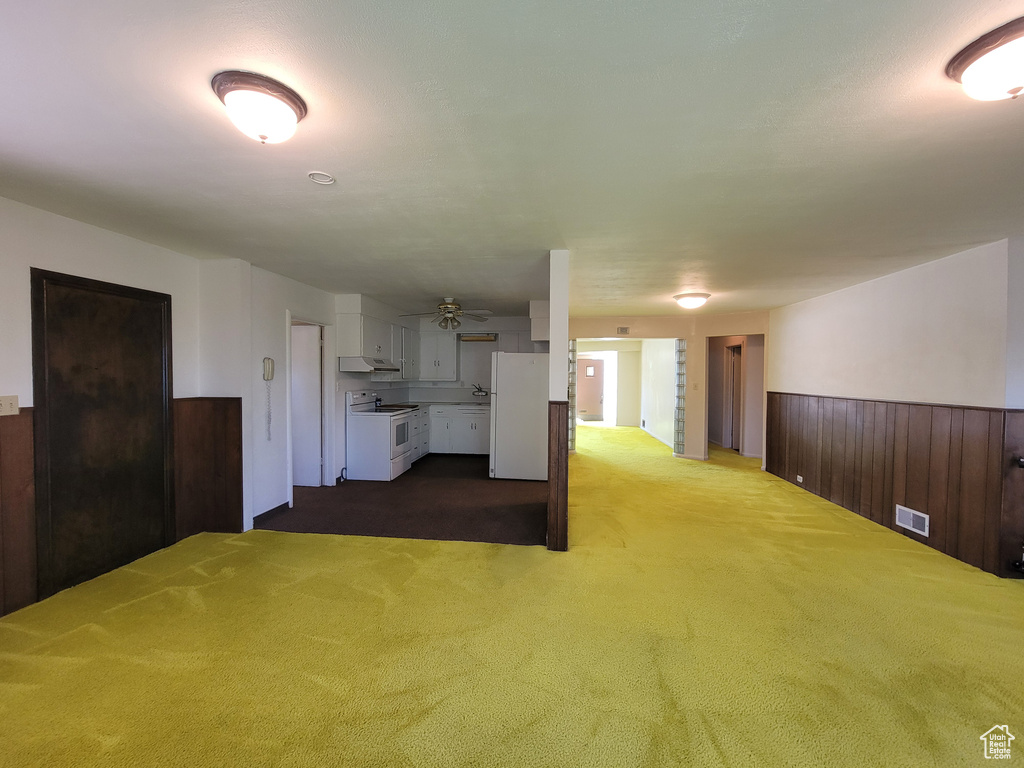 Unfurnished living room featuring carpet, wainscoting, a ceiling fan, and wooden walls