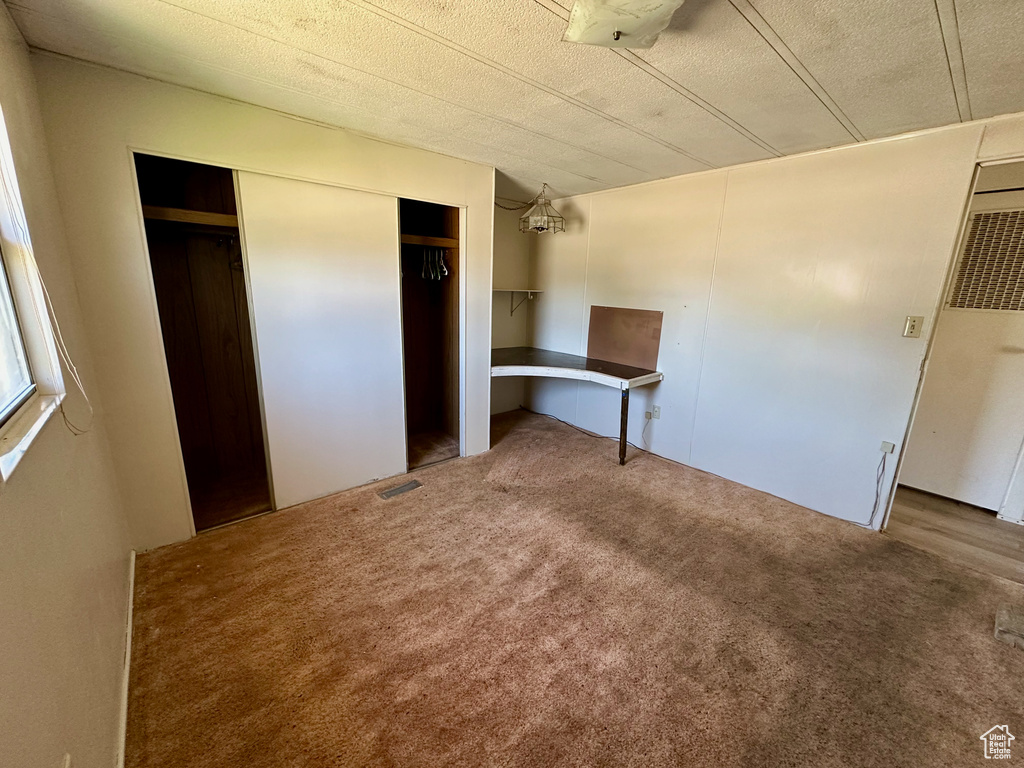 Unfurnished bedroom featuring carpet flooring, a closet, an office area, and a heating unit