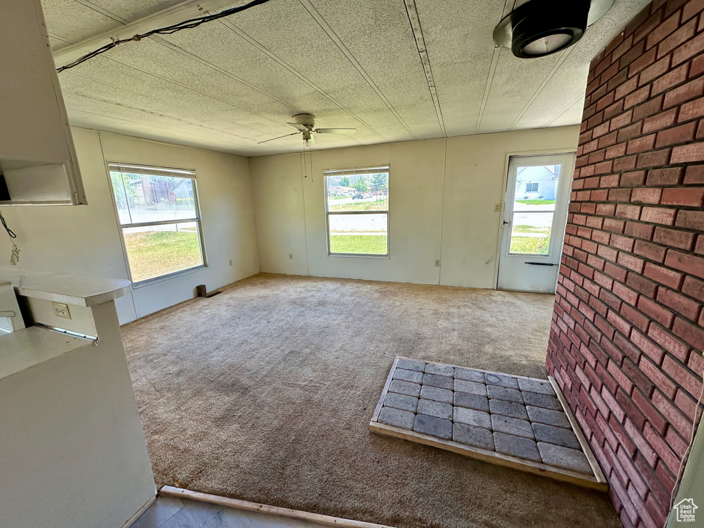 Unfurnished living room featuring healthy amount of natural light, ceiling fan, carpet, and brick wall