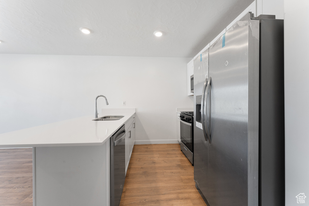 Kitchen featuring appliances with stainless steel finishes, a peninsula, a sink, white cabinetry, and light wood finished floors