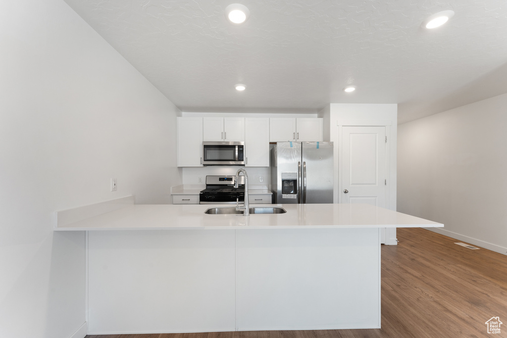 Kitchen featuring appliances with stainless steel finishes, a sink, a peninsula, white cabinetry, and wood finished floors