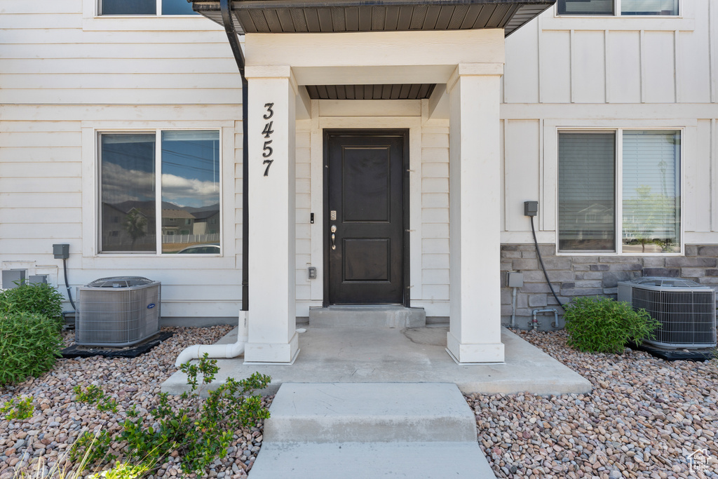 View of exterior entry with central AC unit, board and batten siding, and stone siding