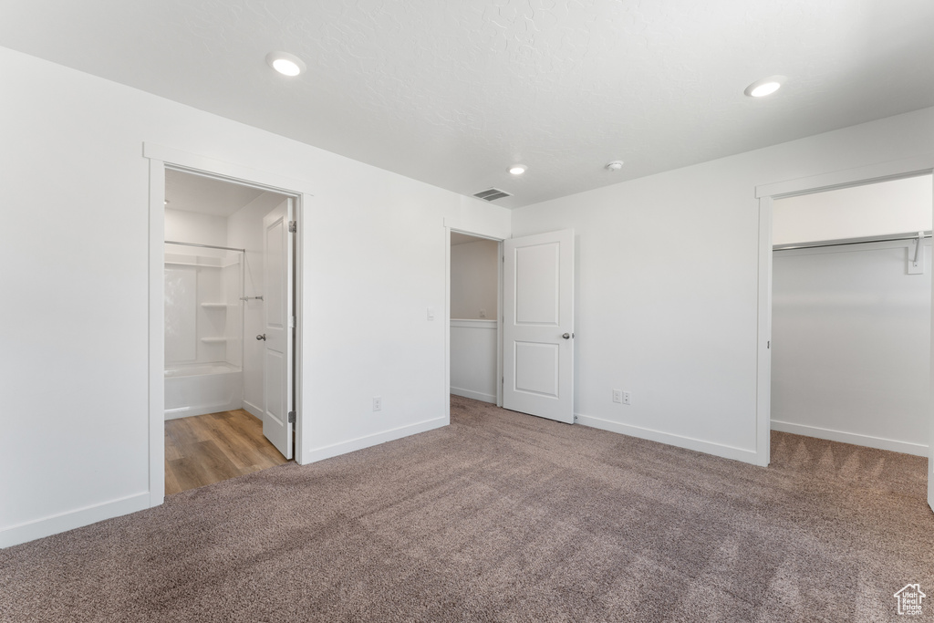 Unfurnished bedroom featuring carpet flooring, baseboards, recessed lighting, a walk in closet, and ensuite bath