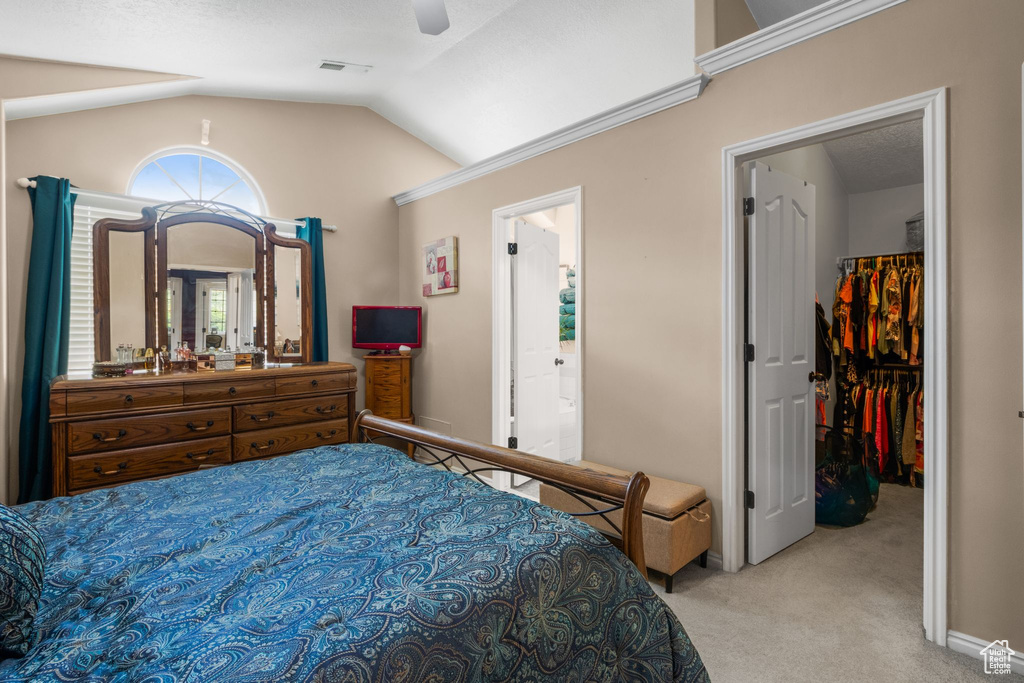 Carpeted bedroom featuring a spacious closet, vaulted ceiling, ceiling fan, a closet, and ensuite bath