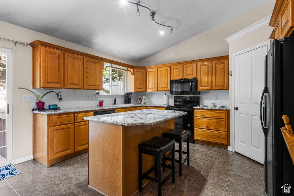 Kitchen with black appliances, vaulted ceiling, a sink, a kitchen island, and brown cabinets
