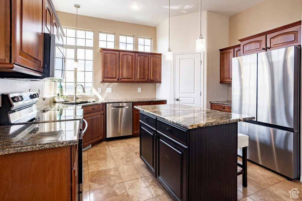 Kitchen with appliances with stainless steel finishes, dark stone countertops, pendant lighting, a breakfast bar area, and a sink