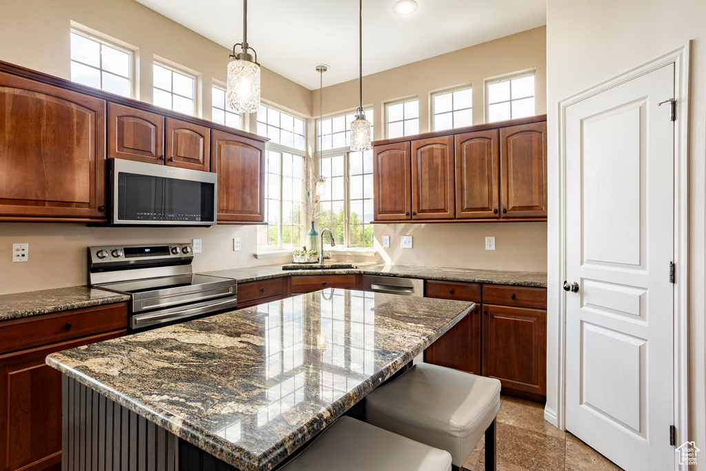 Kitchen featuring appliances with stainless steel finishes, a sink, dark stone countertops, a breakfast bar area, and decorative light fixtures