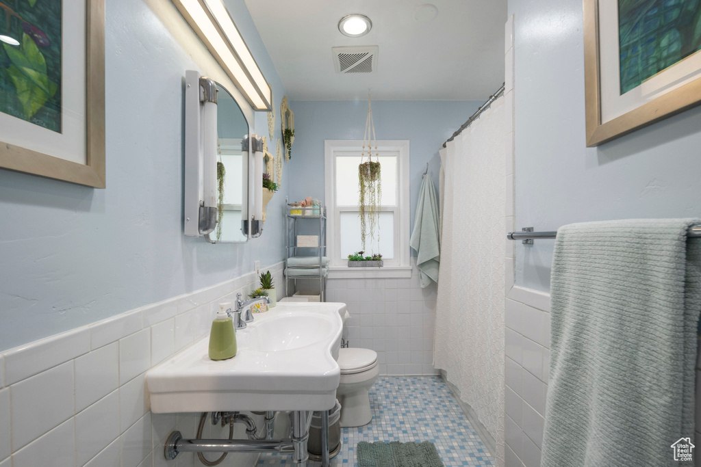 Full bathroom with tile walls, a sink, toilet, tile patterned floors, and a wainscoted wall