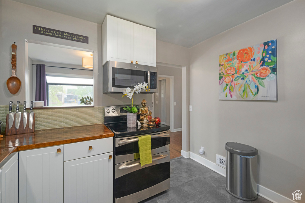 Kitchen with stainless steel appliances, wood counters, decorative backsplash, and white cabinets